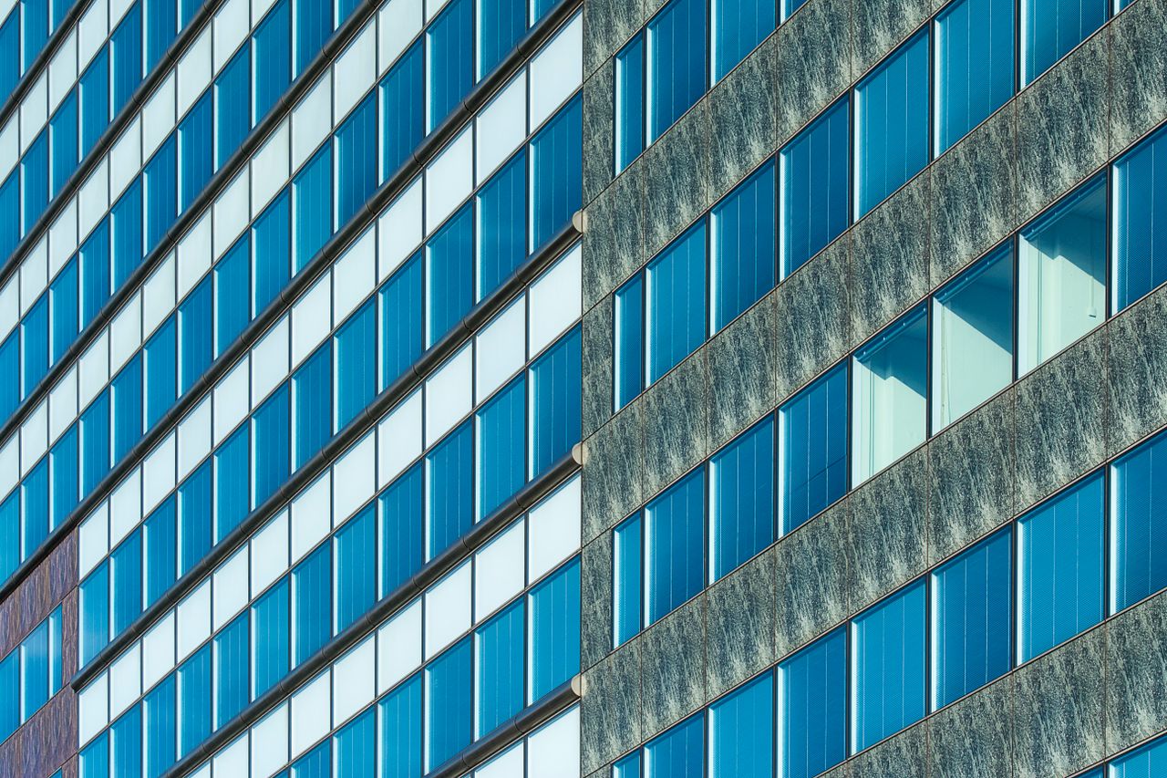 Close-up of a modern glass facade with diagonal lines and windows reflecting blue hues.