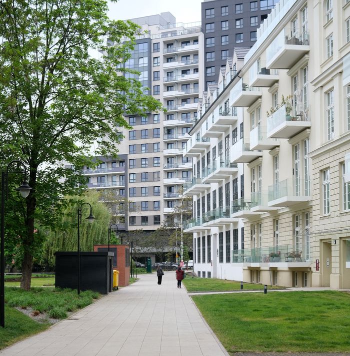 Modern residential buildings with green landscape and walking path, evoking urban living.